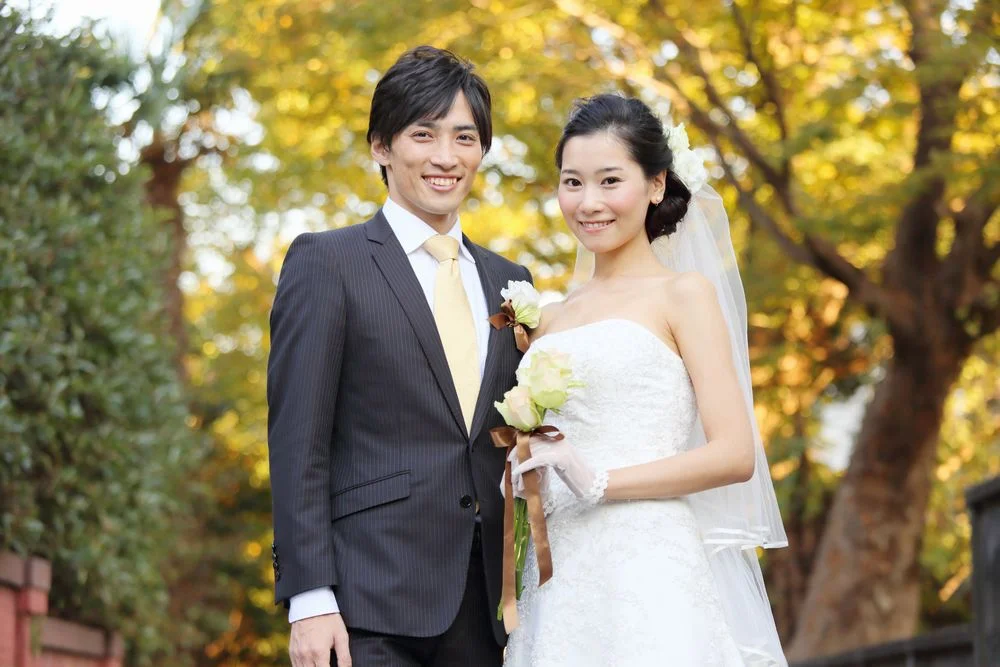 紅葉の木々を背景に、ブーケを手に微笑むウェディング姿の男女